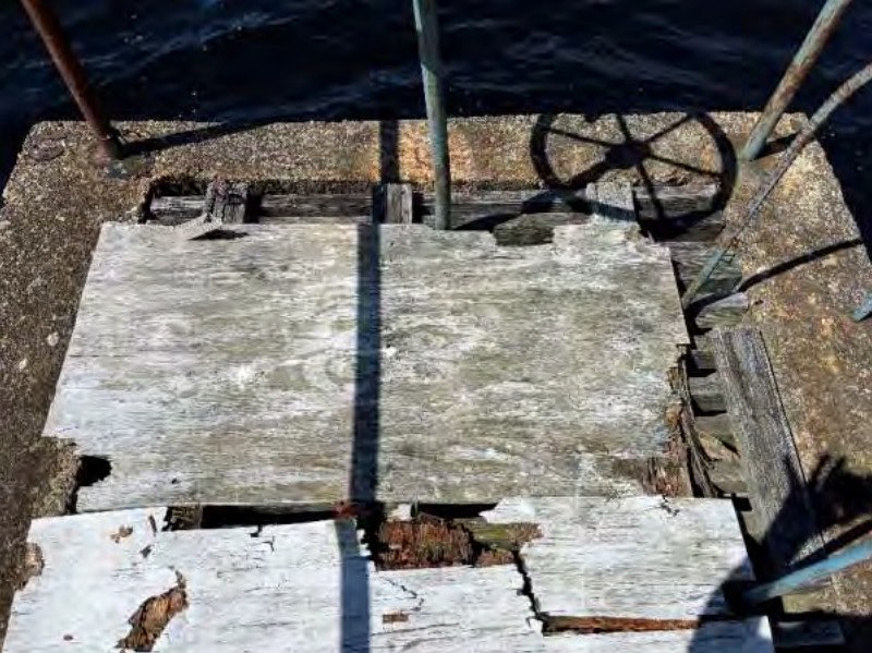 Rotting plywood boards covering the top of the intake structure next to a rusted handwheel